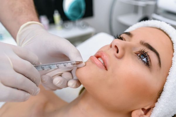 Filler-Injections The doctor cosmetologist makes the Rejuvenating facial injections procedure for tightening and smoothing wrinkles on the face skin of a beautiful, young woman in a beauty salon. The hands of cosmetologist are close-ups that inject hyaluronic acid into the lips of the woman.